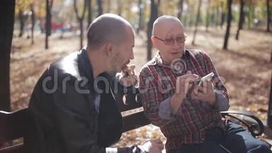 一位年迈的父亲和他成年的儿子坐在公园的长凳上喝咖啡和说话。 年长父亲的成年儿子